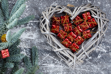 Christmas composition. Christmas gift red boxes in a wicker basket in the shape of a heart, fir branches on a gray aged background, flatlay