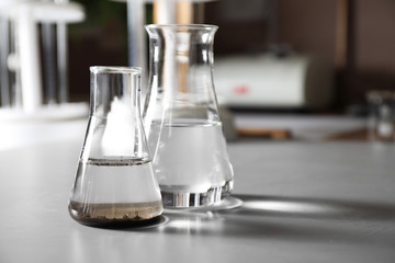 Glassware with soil extract and water on grey table, space for text. Laboratory research