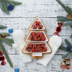 lots of little red gift boxes in the shape of a Christmas tree on a white wooden background. White knitted mittens. Fir branches on the edge of the frame . The concept of Christmas composition.
