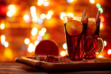 Christmas mulled wine red in a glass with a stick of cinnamon and a piece of orange on a background of twinkling lights