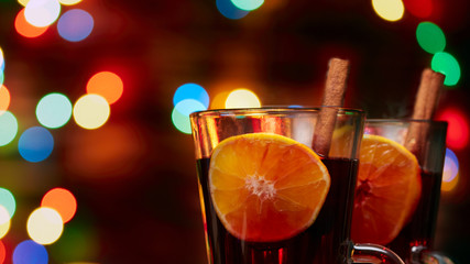 Christmas mulled wine red in a glass with a stick of cinnamon and a piece of orange on a background of twinkling lights