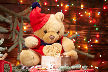 Christmas composition. Teddy bear in a red hat holding a box of homemade cookies on the background of lights Christmas garland on the branches of the Christmas tree. brown wooden background