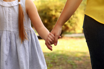 Little girl and her mother holding hands outdoors, closeup. Family weekend