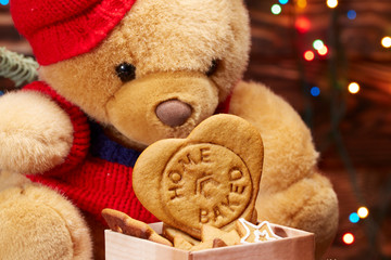 homemade ginger cookies in a wooden box in front of the bear, on the background of defocused lights of the Christmas tree, garlands. Christmas and new year theme. brown background. close up
