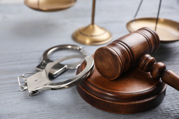 Gavel, handcuffs and scales of justice on grey wooden table, closeup. Criminal law