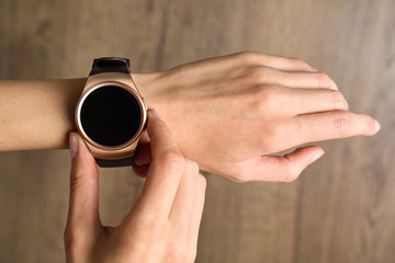 Young woman checking smart watch on blurred wooden background, closeup