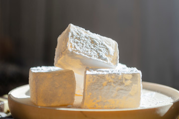 Delicious white traditional bulgarian turkish delight on wooden dish sprinkled with icing sugar like snow. Oriental pieces of sweets for tea close-up. Winter Christmas dessert in the bright sunshine