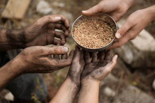 Woman giving poor homeless people bowl of wheat outdoors, closeup