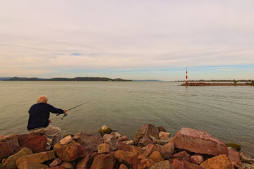 Senior man is fishing  at the marine entrance. Stunning view of lake Bataton. Classic wide angle...