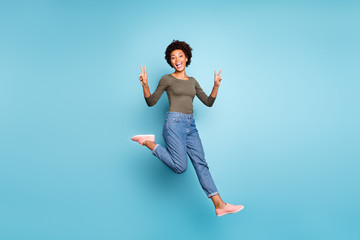 Fototapeta premium Full length body size photo of cheerful funny screaming friendly nice dark skinned woman jumping jeans denim green sweater showing you v-sign isolated over vivid color blue background running