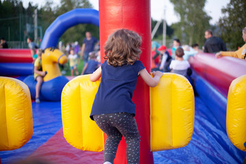 Fototapeta na wymiar A child in an amusement park. Inflatable playground. Children have fun on the street. Girl jumping on an inflatable structure.