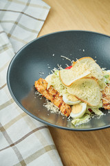 Caesar salad with croutons, parmesan, chicken, egg in a black stylish bowl. Restaurant serving. Selective focus, wooden background
