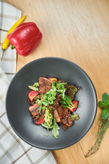 Grilled veal salad with lettuce, cherry tomatoes, dor blue cheese in a black bowl on wooden background. Selective focus, c;ose up