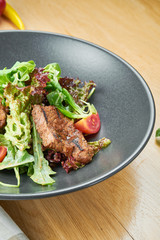 Grilled veal salad with lettuce, cherry tomatoes, dor blue cheese in a black bowl on wooden background. Selective focus, c;ose up