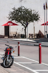 moto garée sur le trottoir en fond des parasols