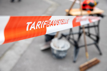 Tarifbaustelle als Schriftzug auf einem Sperrband vor Arbeitsmitteln einer Baustelle
