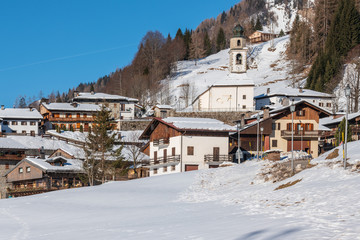 Fototapeta na wymiar Winter in Sauris di Sotto. Traditional architecture under the sun and snow