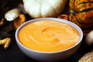 Roasted pumpkin and carrot soup with cream and pumpkin seeds on wooden background.