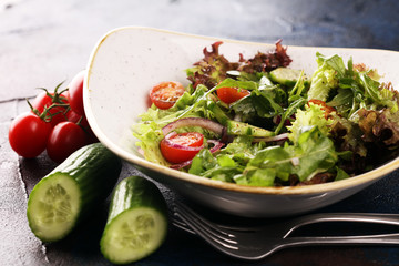 bowl of salad with vegetables and greens, with tomato, cucumber and onions on rustic table