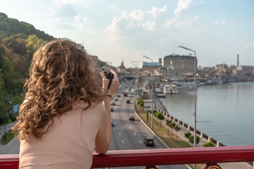 Young woman on the bridge taking photo of the city at summer with digital camera. 