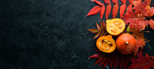 Autumn vegetables. Pumpkin with pumpkin seeds and autumn leaves. flat lay. On a black stone background. Top view. Free space for your text.