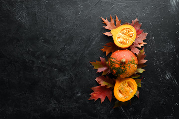 Autumn vegetables. Pumpkin with pumpkin seeds and autumn leaves. flat lay. On a black stone background. Top view. Free space for your text.