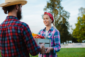 A man and a woman holding a box with a crop of farm vegetables background of the garden.