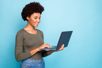 Portrait of positive cool confident afro american girl freelancer use laptop type emails chat with her partners business clients wear green style clothes denim jeans isolated blue color background