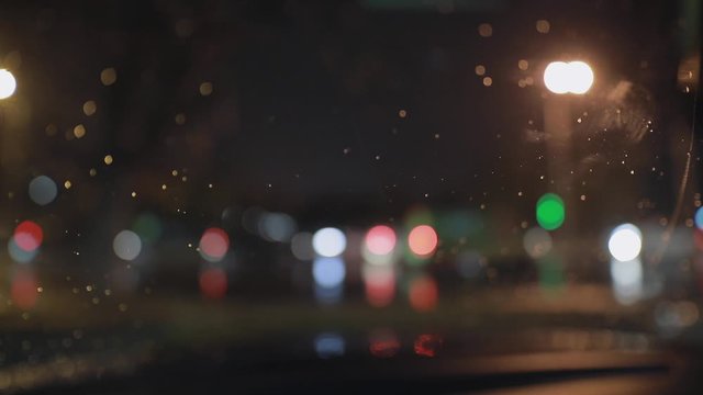 Beautiful background of front car window in raindrops cleaning by windscreen wiper at late night