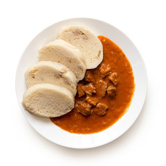 Beef goulash with bread dumplings on white ceramic plate isolated on white. Top view.