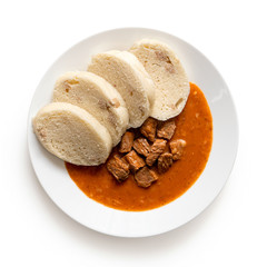 Beef goulash with bread dumplings on white ceramic plate isolated on white. Top view.