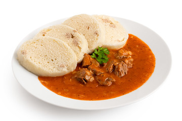 Beef goulash with bread dumplings and parsley garnish on white ceramic plate isolated on white.