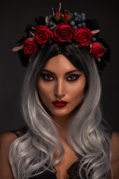 Creative image of Halloween makeup look or Dia De Los Muertos holiday on dark background with copyspace. Beautiful Model with red hear wearing a headdresses