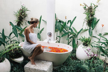 Woman relaxing in outdoor bath with flowers in Bali spa hotel.