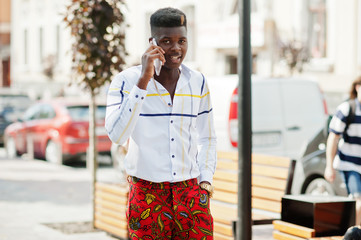 Obraz premium Portrait of handsome stylish african american model man in red throusers and white shirt with cell phone at hand.