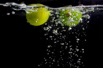 Fototapeta na wymiar Green limes in water on a black background.