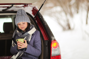 Caucasian woman with hot mug in the car trunk