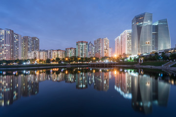 Fototapeta na wymiar Buildings with reflections on lake at twilight at Thanh Xuan park. Hanoi cityscape at twilight period