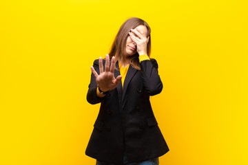 young pretty businesswoman covering face with hand and putting other hand up front to stop camera,...