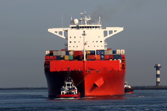 rotes Containerschiff mit Schleppern