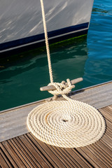 Mooring rope arrange in circle on wooden pier with blue water background, vertical composition
