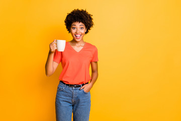 Fototapeta na wymiar Photo of charming cute cheerful nice attractive girlfriend wearing orange t-shirt denim jeans holding cup of tea isolated over yellow vivid color background