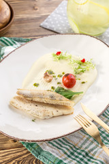 portion of golden fried sea fish served on white plate with mashed potato and tomato on wooden table
