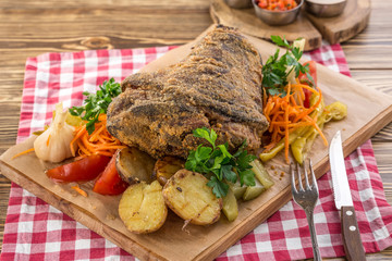 Pork knuckle roast served with potato and pickled vegetables and glass of beer on wooden table