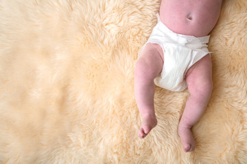 Newborn baby legs with white nappy, diaper on a fur background.