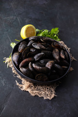 Bowl with fresh raw mussels on dark background
