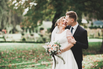 Stylish couple of happy newlyweds walking in the park on their wedding day with bouquet