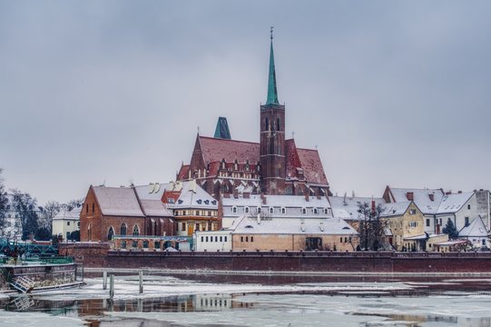 zimowy krajobraz Wrocławia stolicy Śląska, rzeka Odra wyjątkowo skuta lodem, widok na Ostr&oacute;w Tumski z gotyckim kościołem Świętego Krzyża