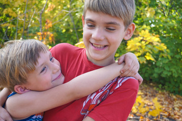 The younger brother hugs the older one and looks at him, two loving brothers are standing in an...