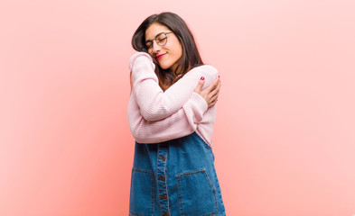 young  pretty woman feeling in love, smiling, cuddling and hugging self, staying single, being selfish and egocentric against pink background. - obrazy, fototapety, plakaty